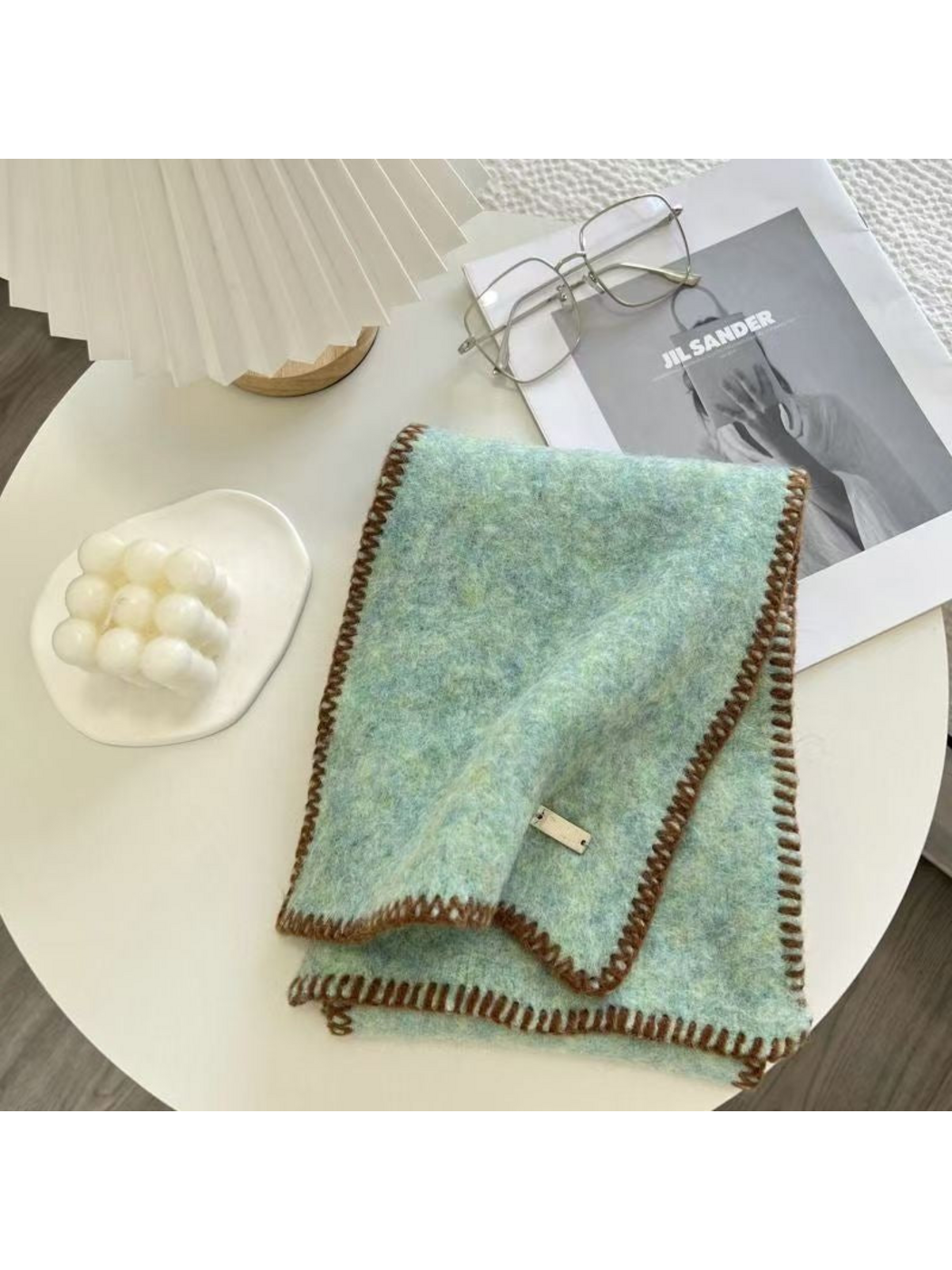Mint scarf folded on a table with brown blanket-stitched edges