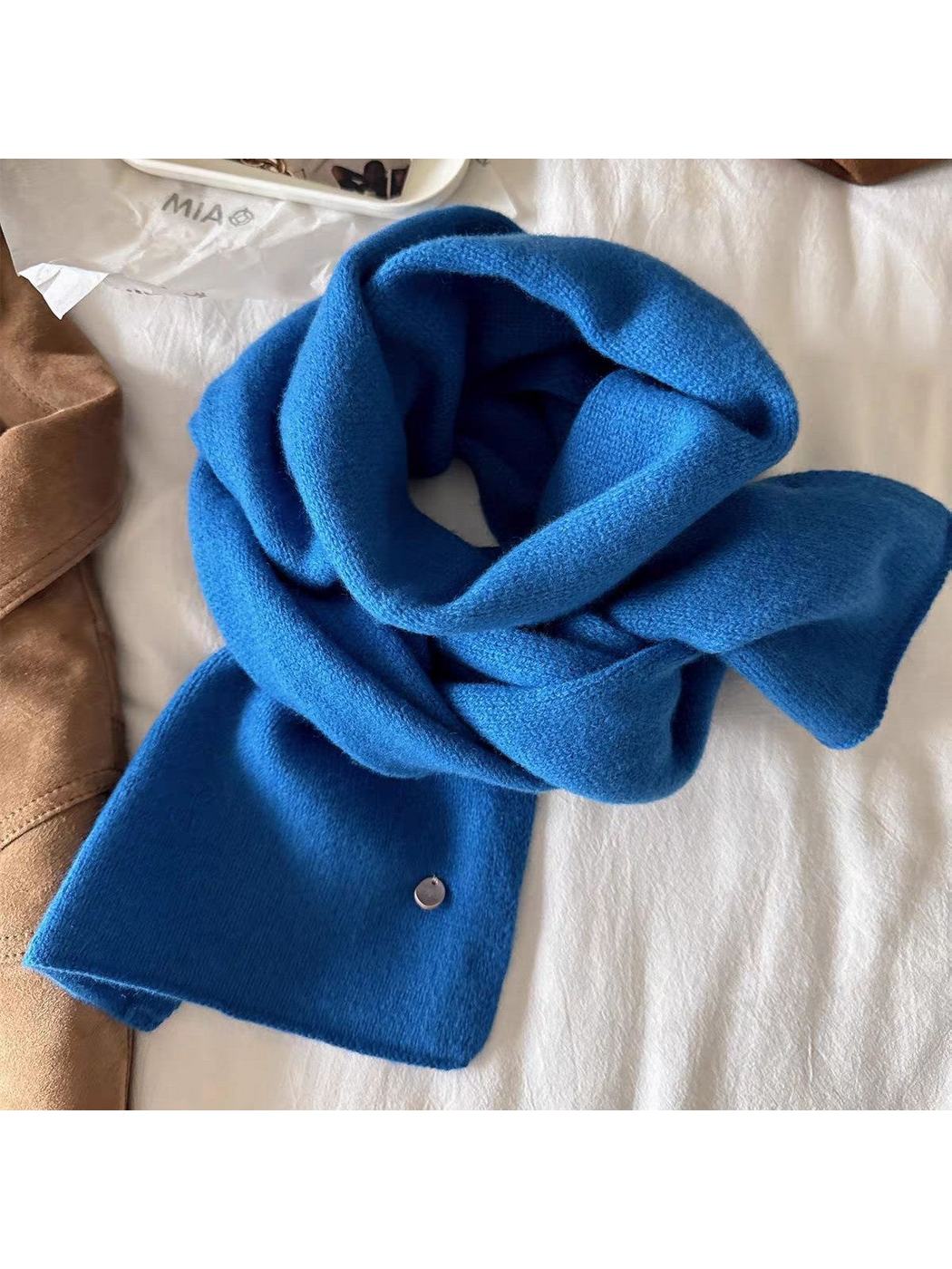 Blue scarf close-up showing knit texture, broad ends and a round disc detail