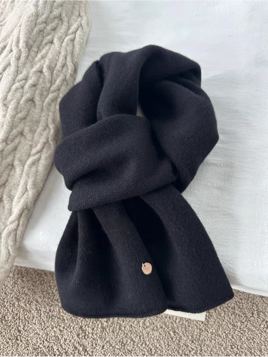 Black scarf in a looped arrangement with broad ends and a round gold-tone disc