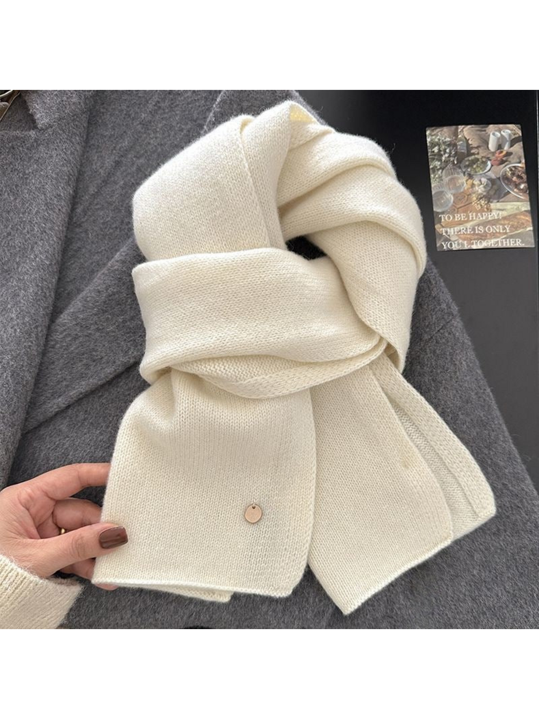Ivory scarf held at one end, showing looped folds and a round gold-tone disc