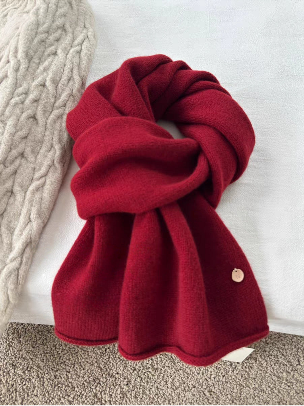 Burgundy scarf in a looped arrangement with broad ends and a round gold-tone disc