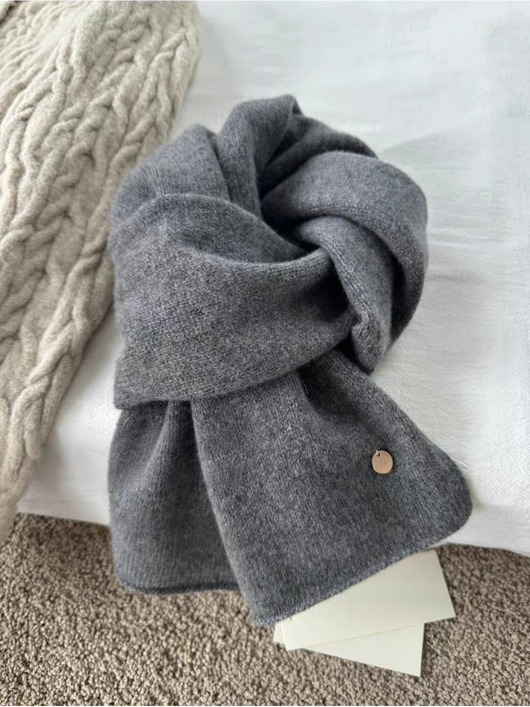 Gray scarf in a looped arrangement showing a heathered surface and round gold-tone disc