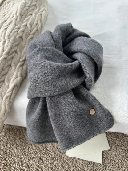 Gray scarf in a looped arrangement showing a heathered surface and round gold-tone disc