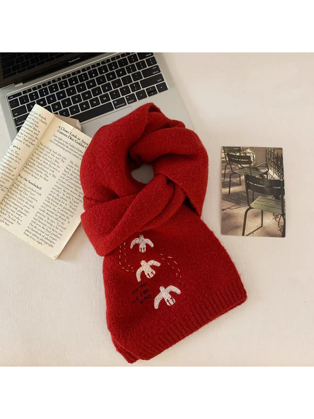 Red bird-embroidered scarf looped on a tabletop beside a book