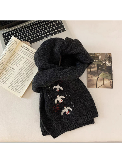 Black bird-embroidered scarf looped on a tabletop beside a book