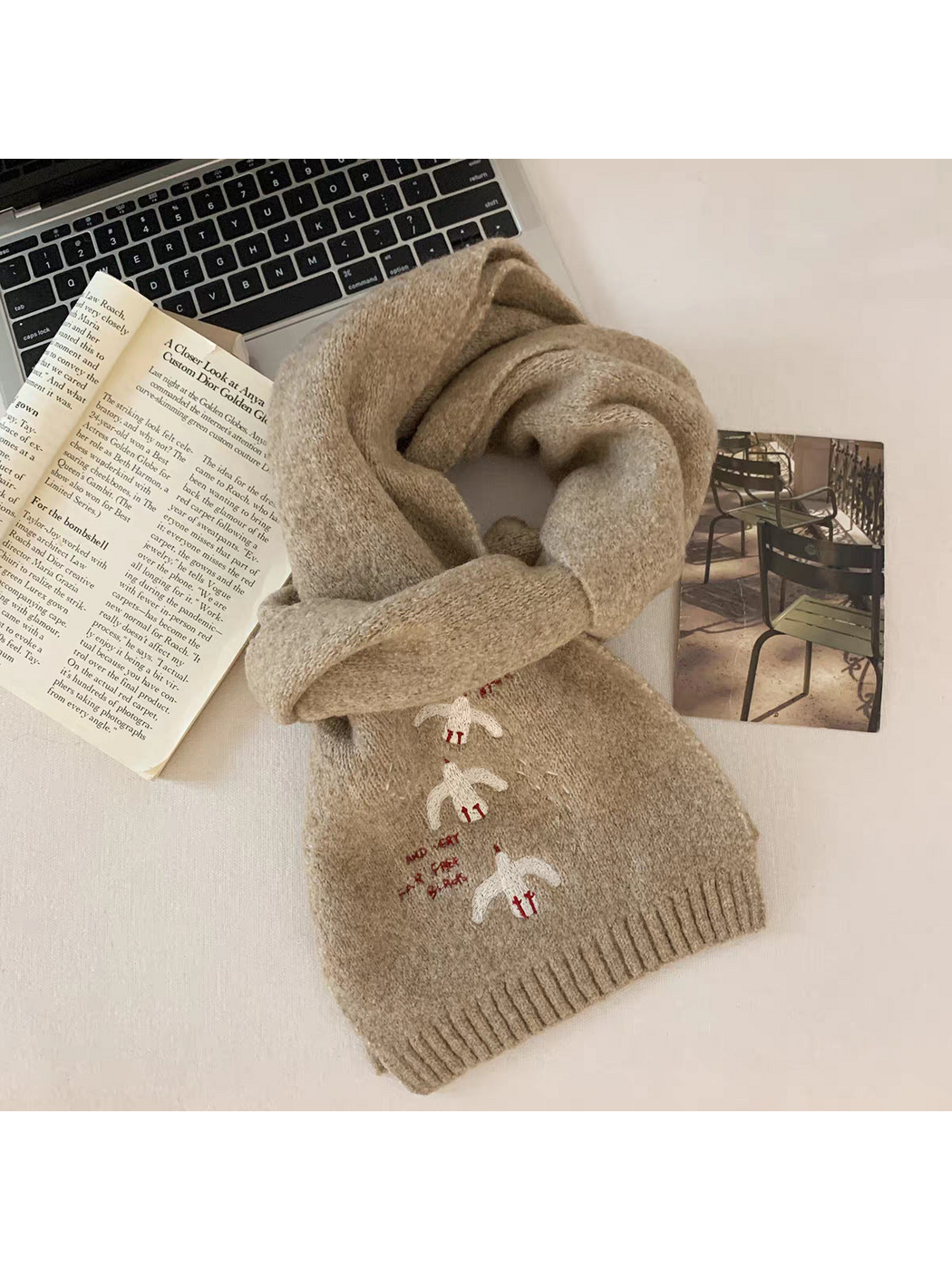 Beige bird-embroidered scarf looped on a tabletop beside a book