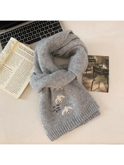 Gray bird-embroidered scarf loosely looped on a tabletop beside a book