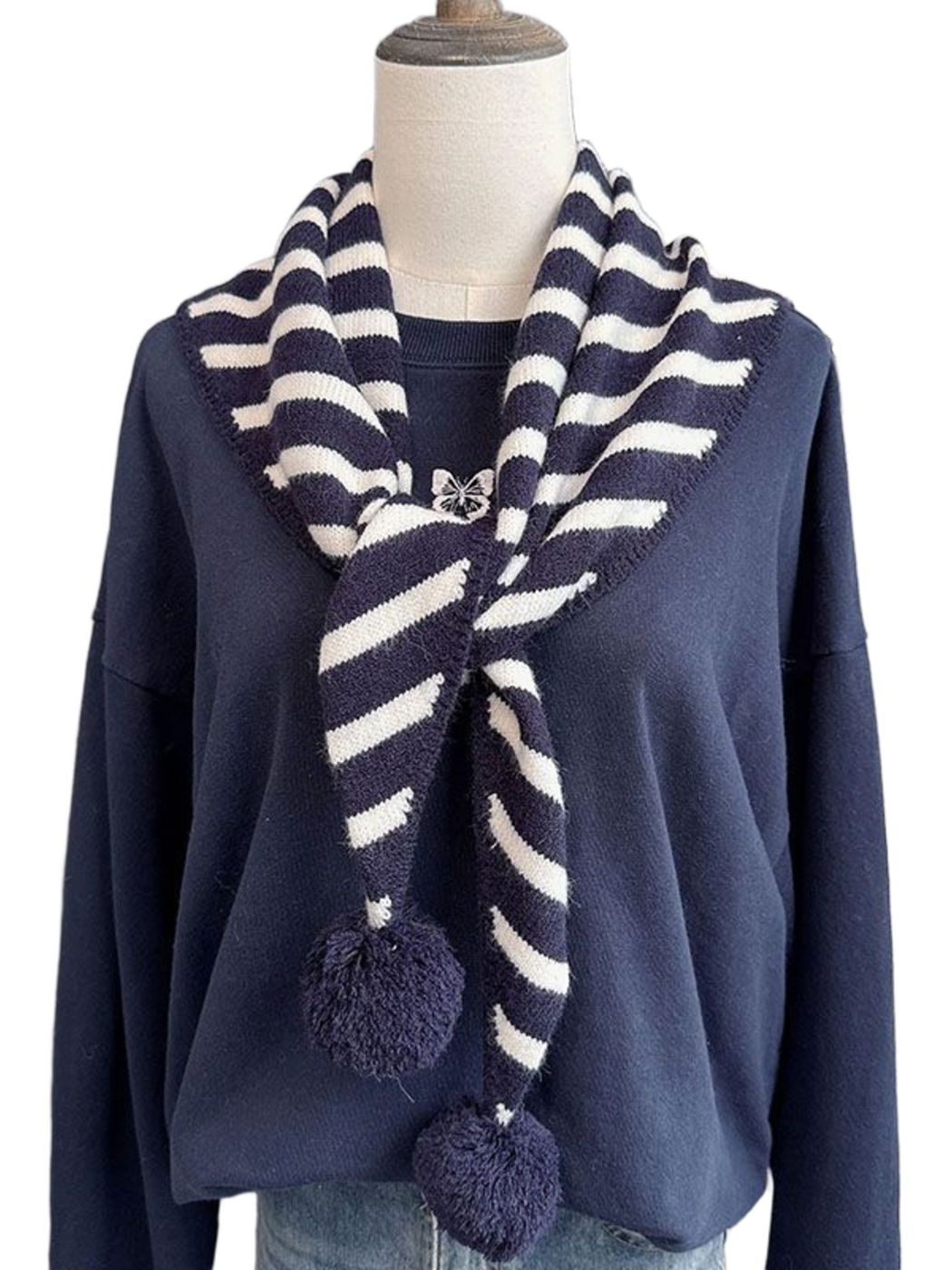 Navy striped triangle scarf with pom-pom ends draped on a mannequin
