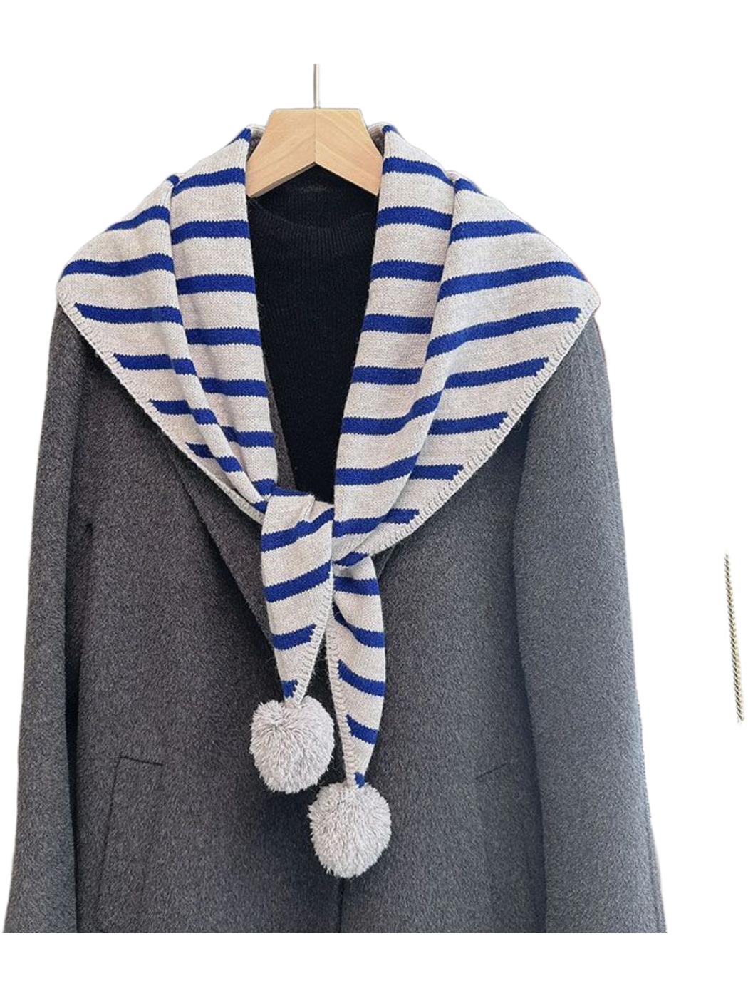 Blue striped triangle scarf with light gray pom-pom ends over a gray coat