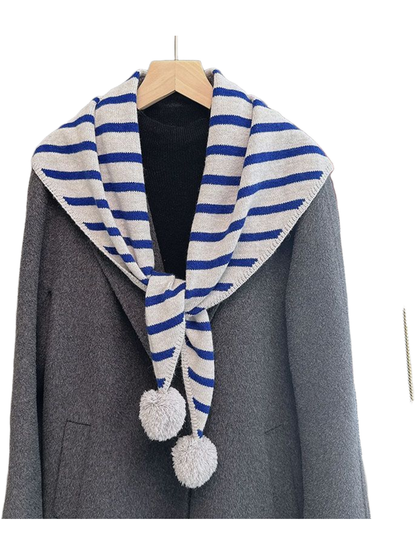 Blue striped triangle scarf with light gray pom-pom ends over a gray coat
