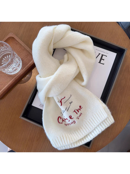 Ivory scarf looped on a tabletop with embroidered skiing figures and ribbed ends
