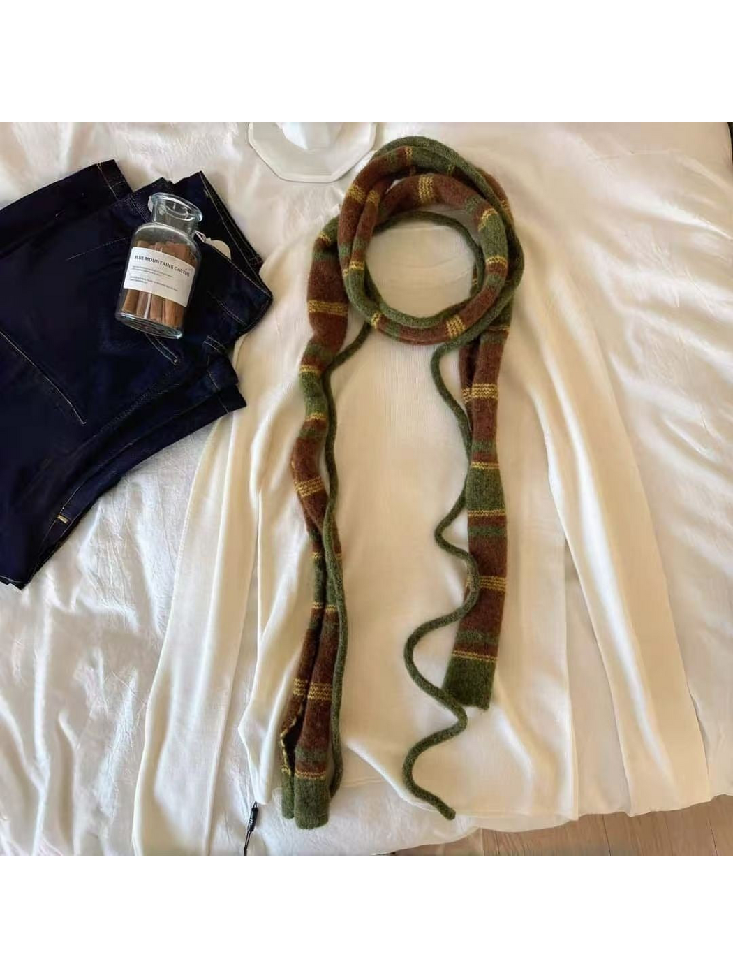 Green striped scarf looped over a cream top with slender green cords visible