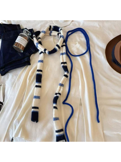 Navy striped scarf and blue cords arranged over a cream top, cropped detail