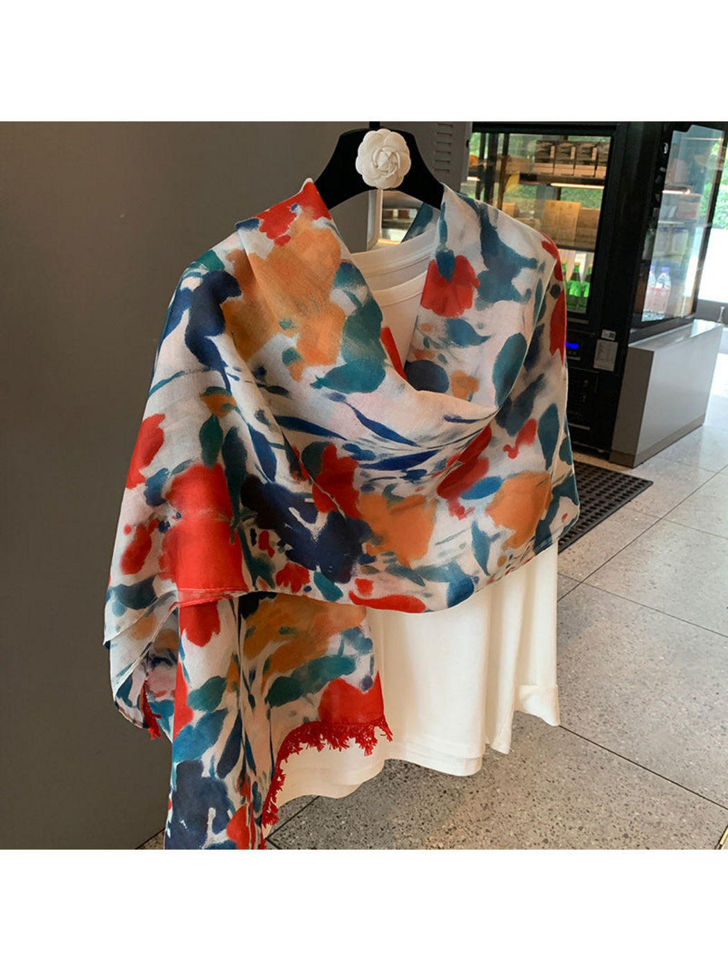 Multicolor floral scarf loosely draped across a white top, with red fringe visible