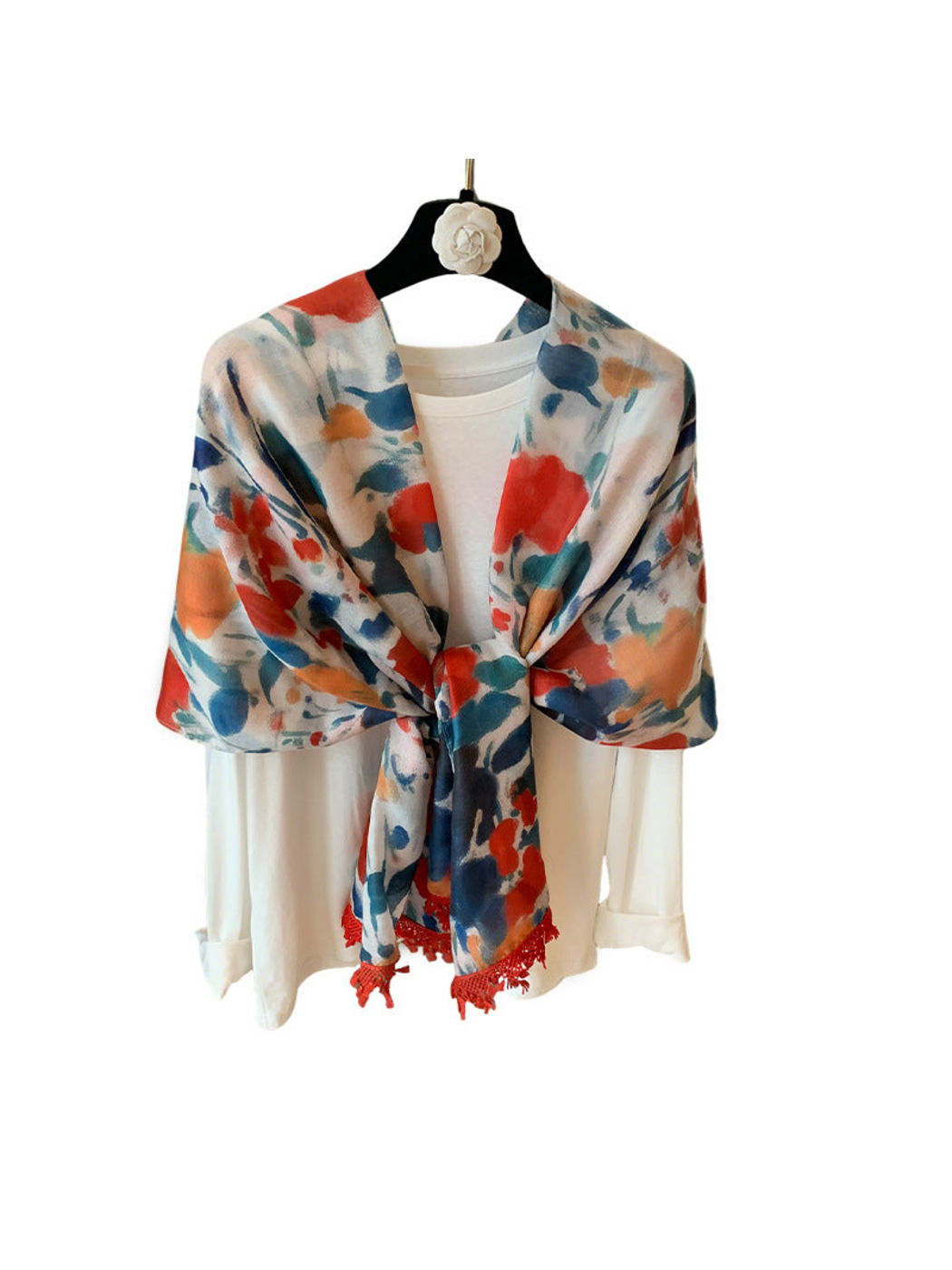 Multicolor floral scarf tied over a white top, with red fringed ends against a white background