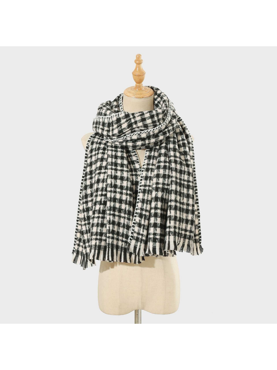 Black plaid scarf with white stitched edging and fringed ends, looped on a mannequin