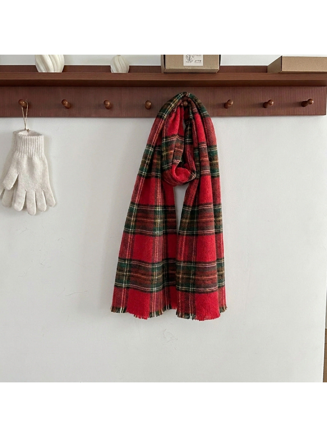 Red tartan plaid scarf looped over a wooden peg, showing short fringed ends
