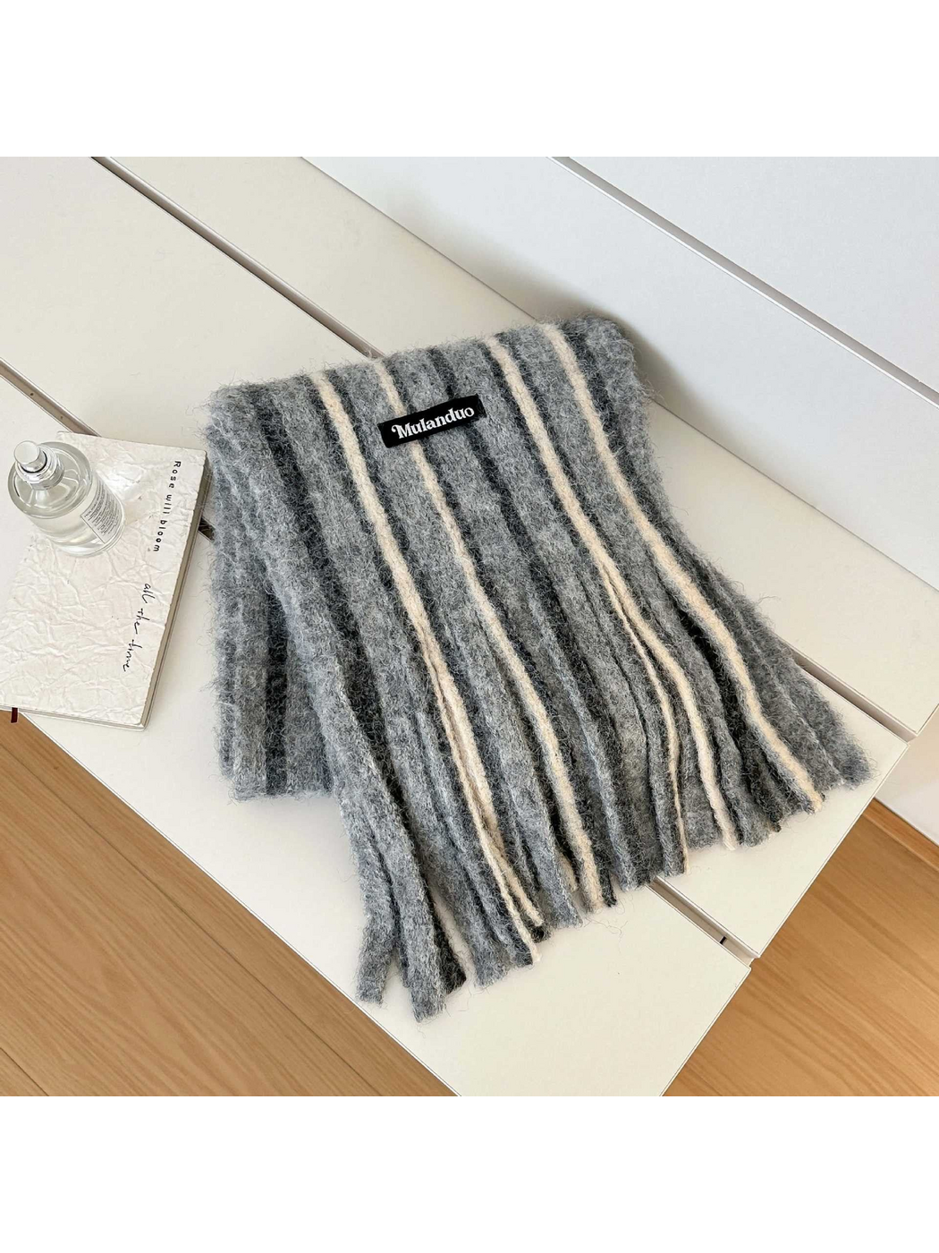 Gray striped scarf with a fuzzy surface and long fringe, folded on a white bench