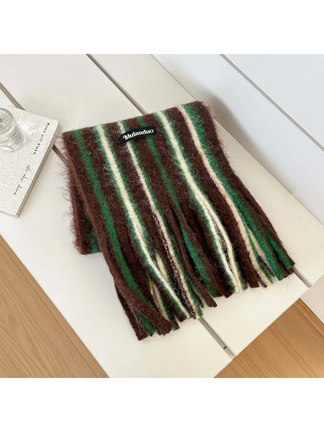 Brown scarf with green and cream stripes and long fringe, folded on a white bench