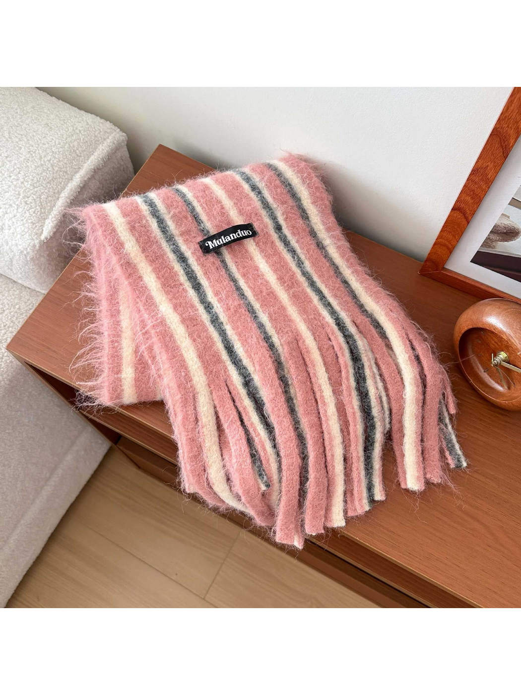 Pink scarf with cream and dark gray stripes and long fringe, draped on a wooden table