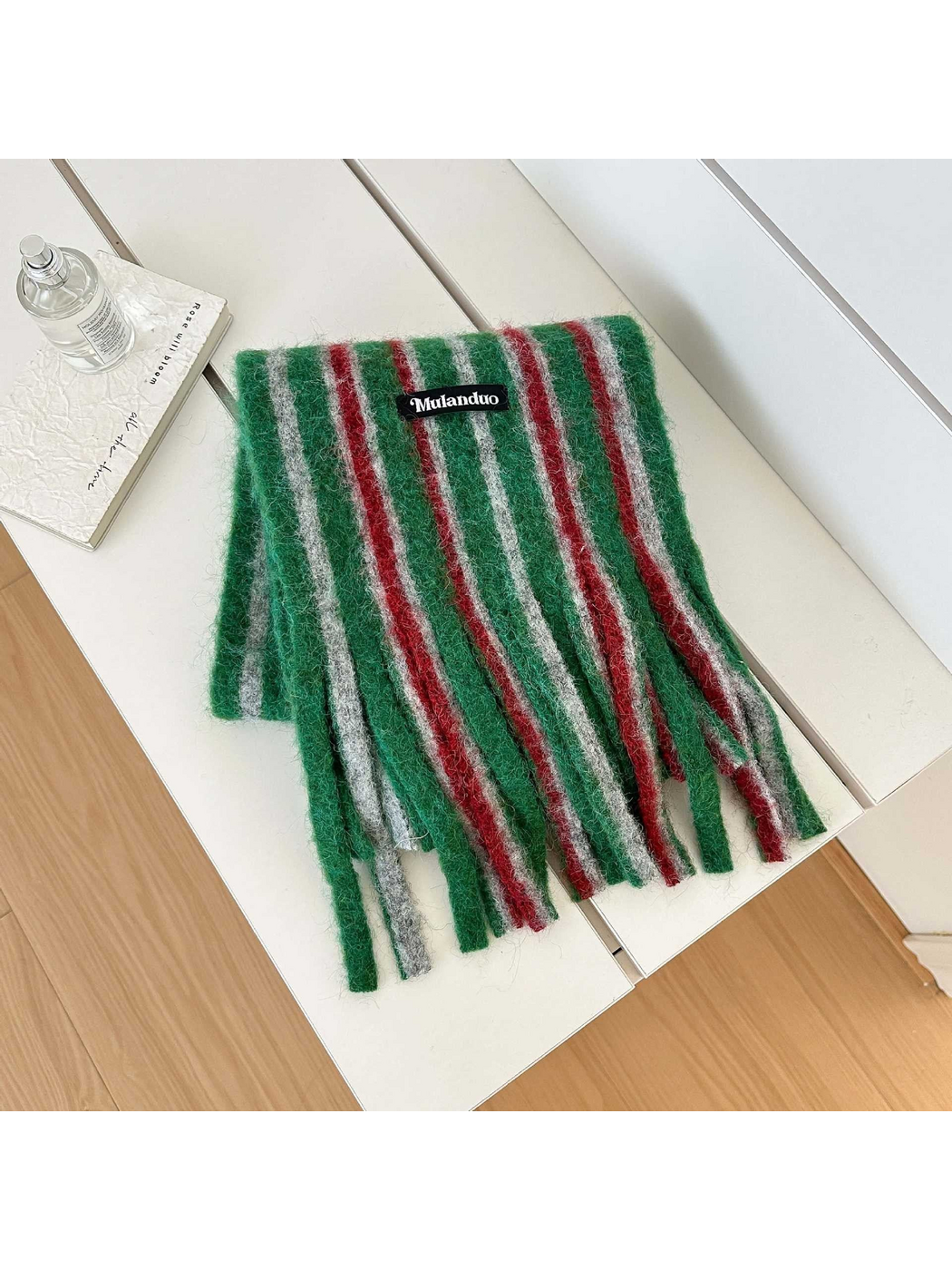 Green scarf with red and gray stripes and long fringe, folded on a white bench