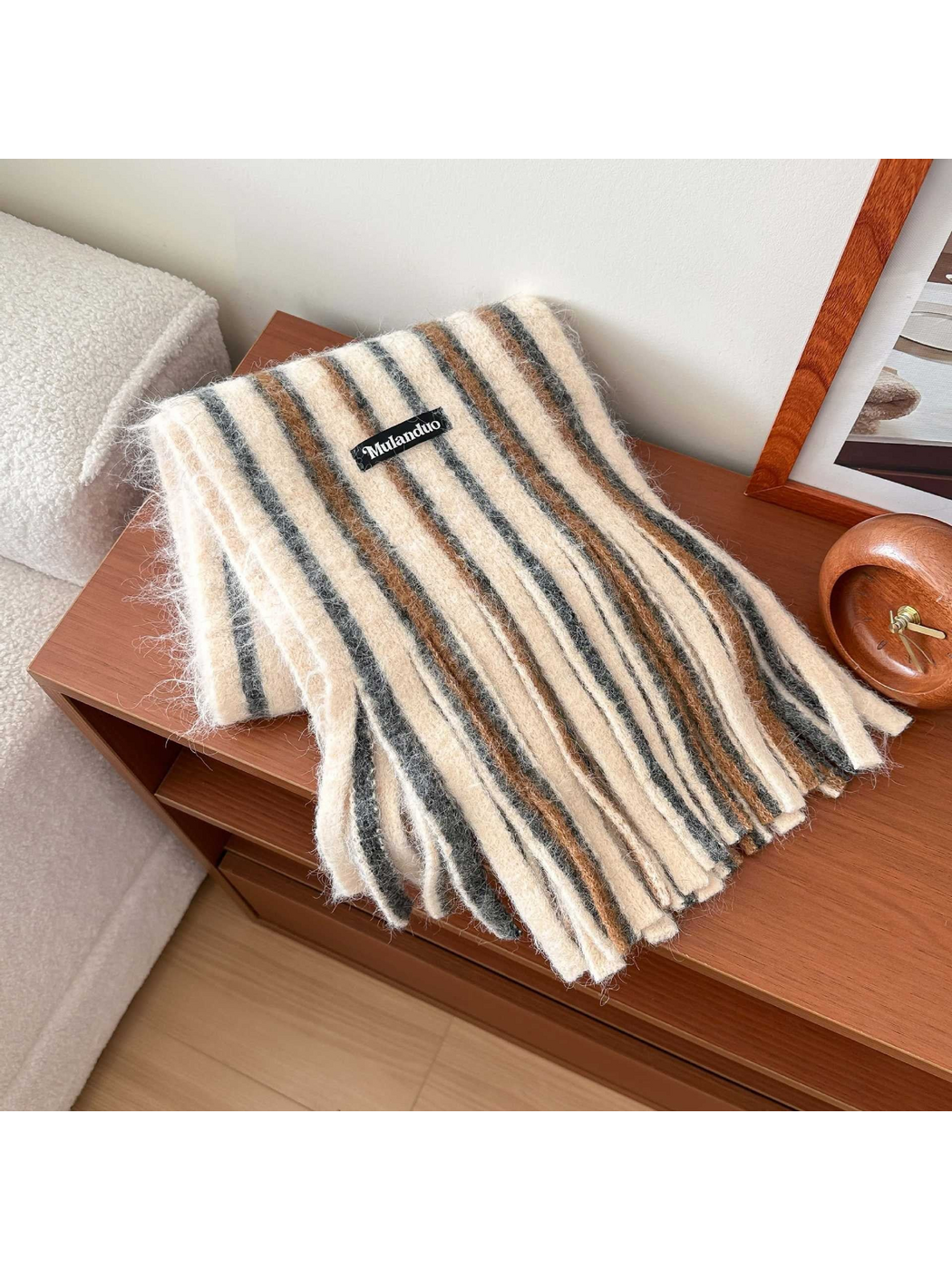 Beige scarf with gray and brown stripes and long fringe, draped on a wooden table