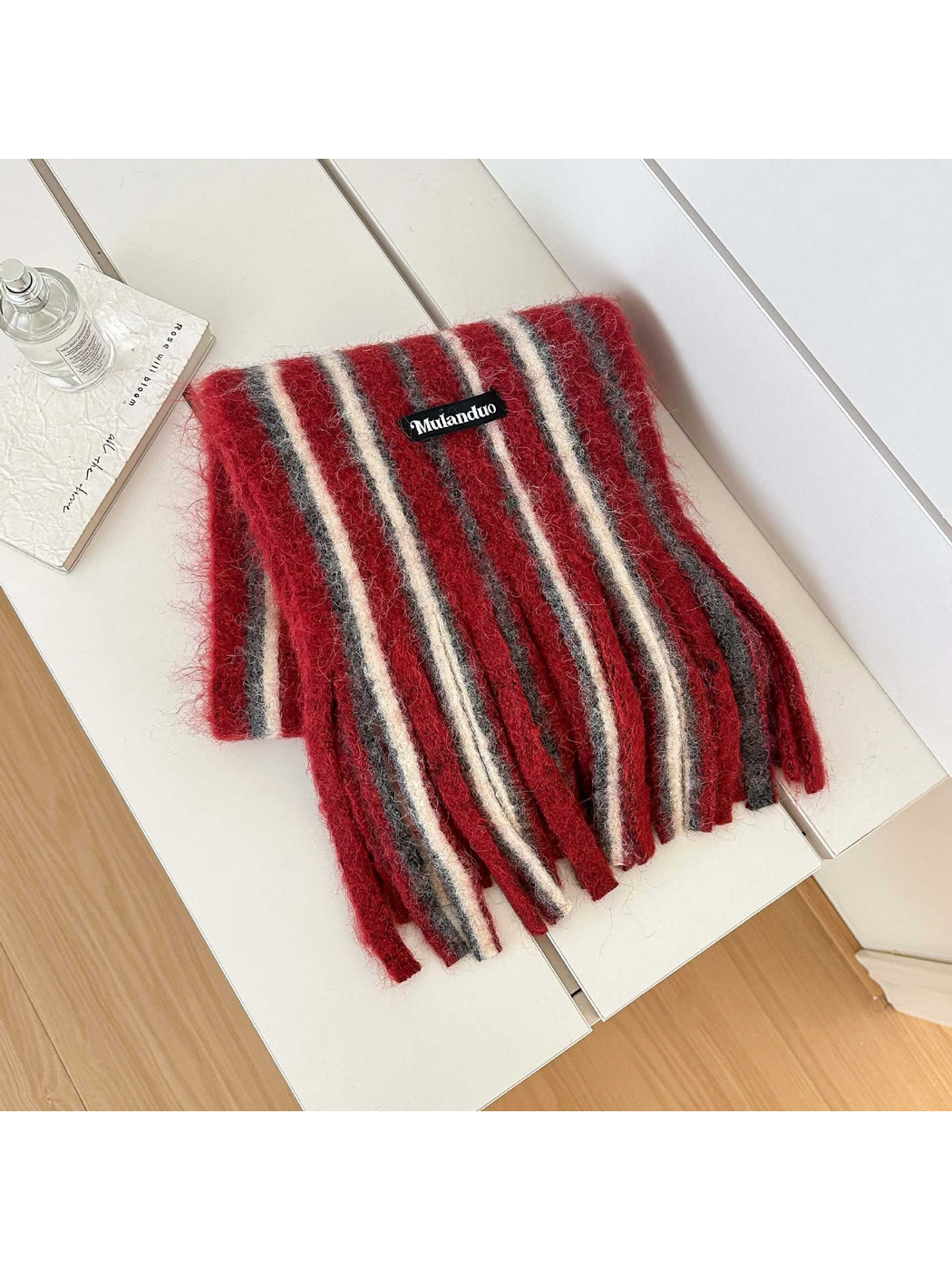 Red scarf with gray and cream stripes and long fringe, folded on a white bench