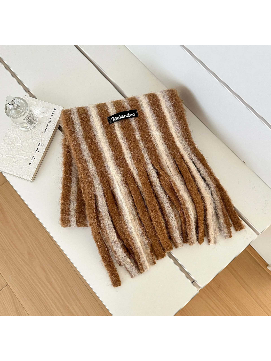 Camel striped scarf with a fuzzy surface and long fringe, folded on a white bench