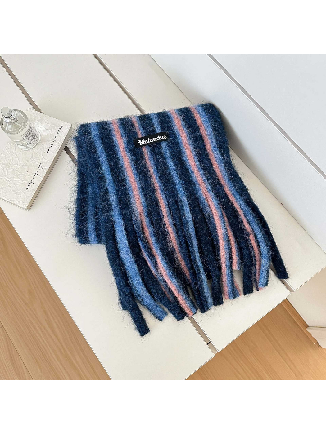 Blue scarf with blue and pink stripes and long fringe, folded on a white bench