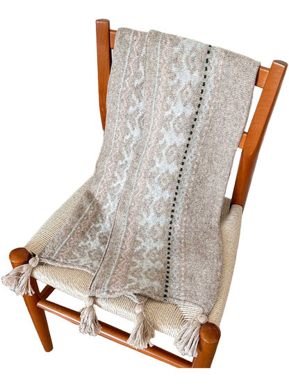 Beige scarf with pale blue deer motifs, a dark green dotted line and corner tassels, draped over a chair