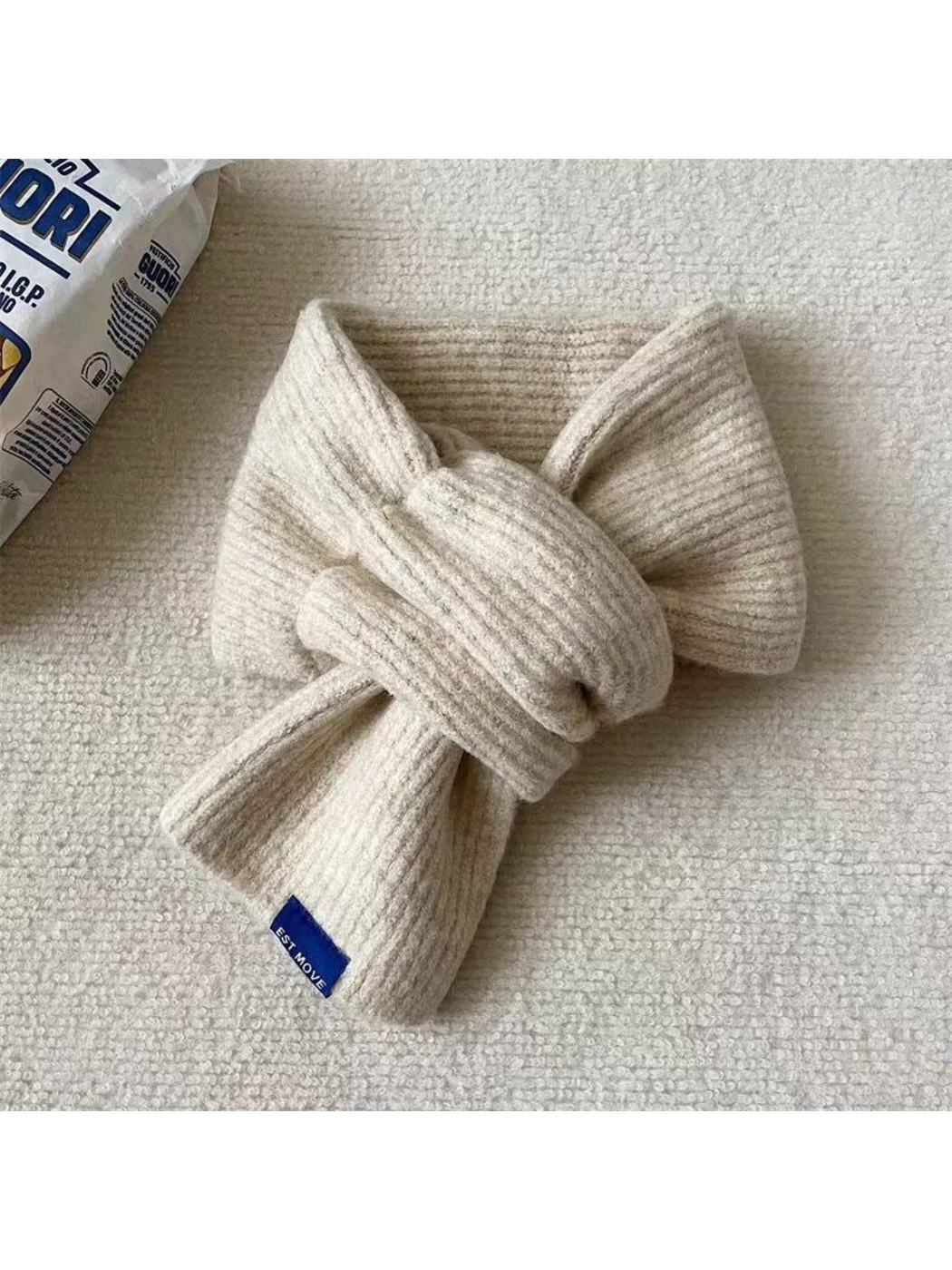 Ivory ribbed scarf in a crossover arrangement with a blue end label