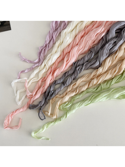 Close-up of pastel crinkled scarves with twisted ends on a pale surface