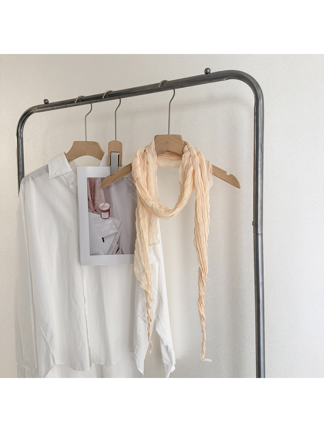 Beige crinkled scarf looped on a wooden hanger with long tapered ends