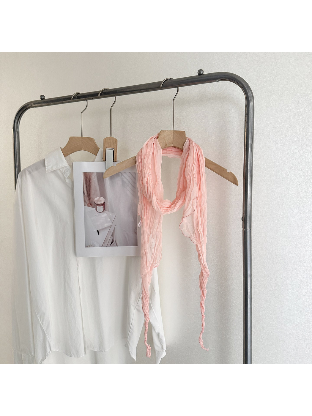 Pink crinkled scarf looped on a wooden hanger with long tapered ends
