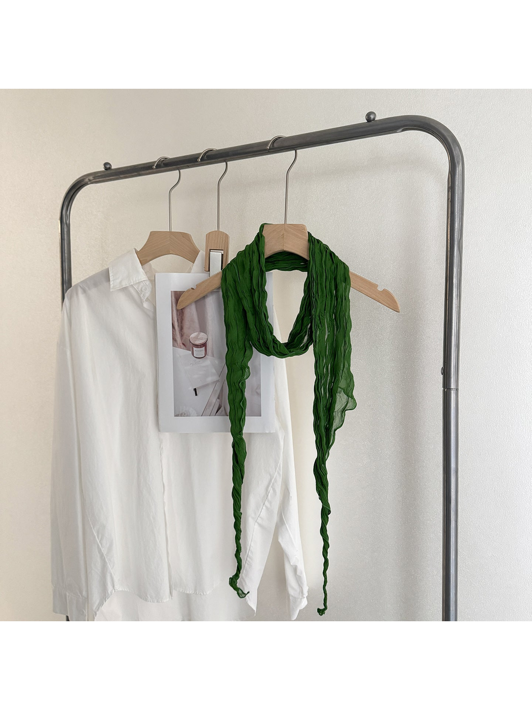 Green crinkled scarf looped on a wooden hanger with long tapered ends