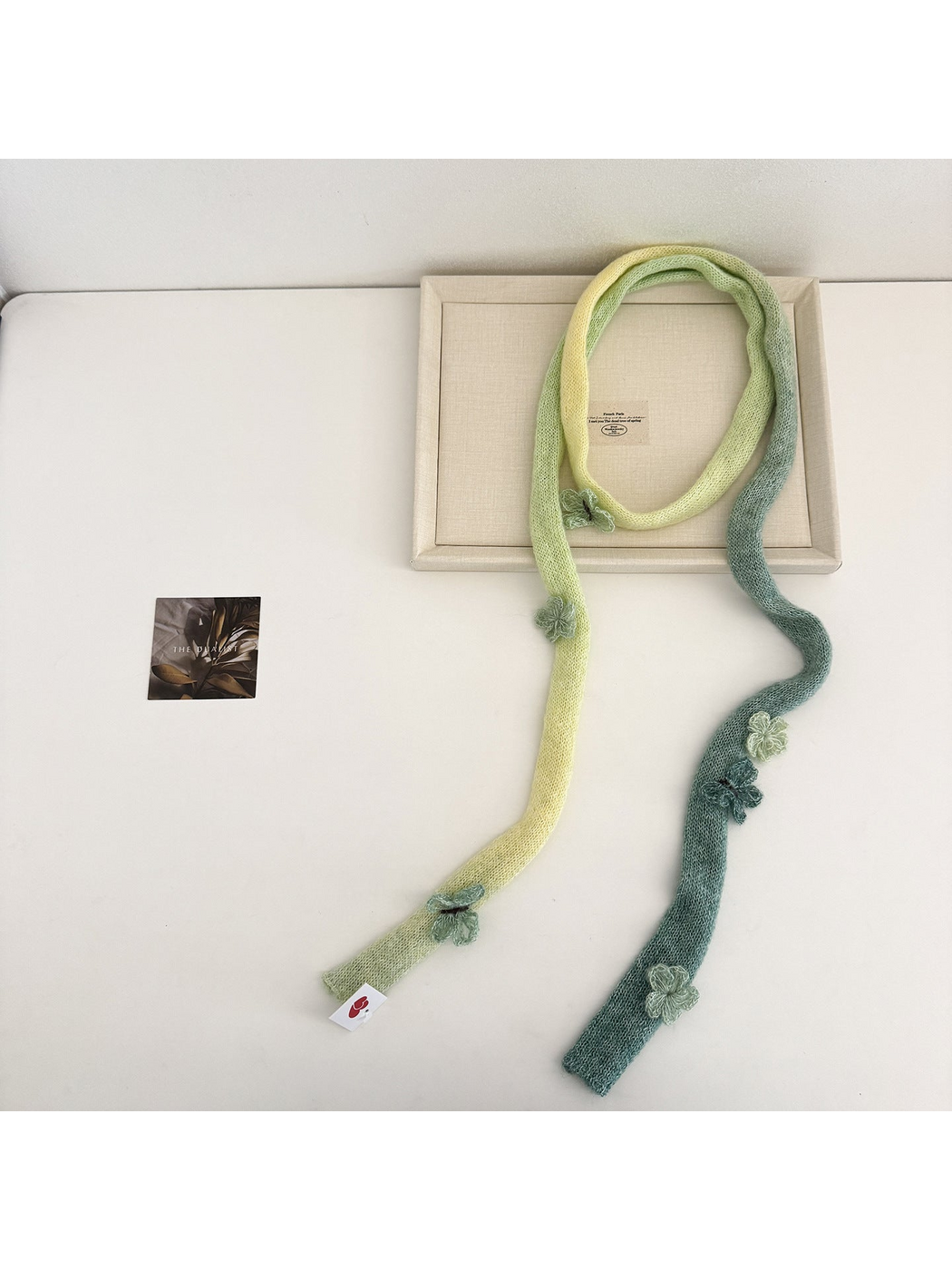 Green knit scarf arranged in a long loop with flower and butterfly embellishments