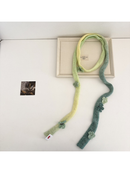 Green knit scarf arranged in a long loop with flower and butterfly embellishments