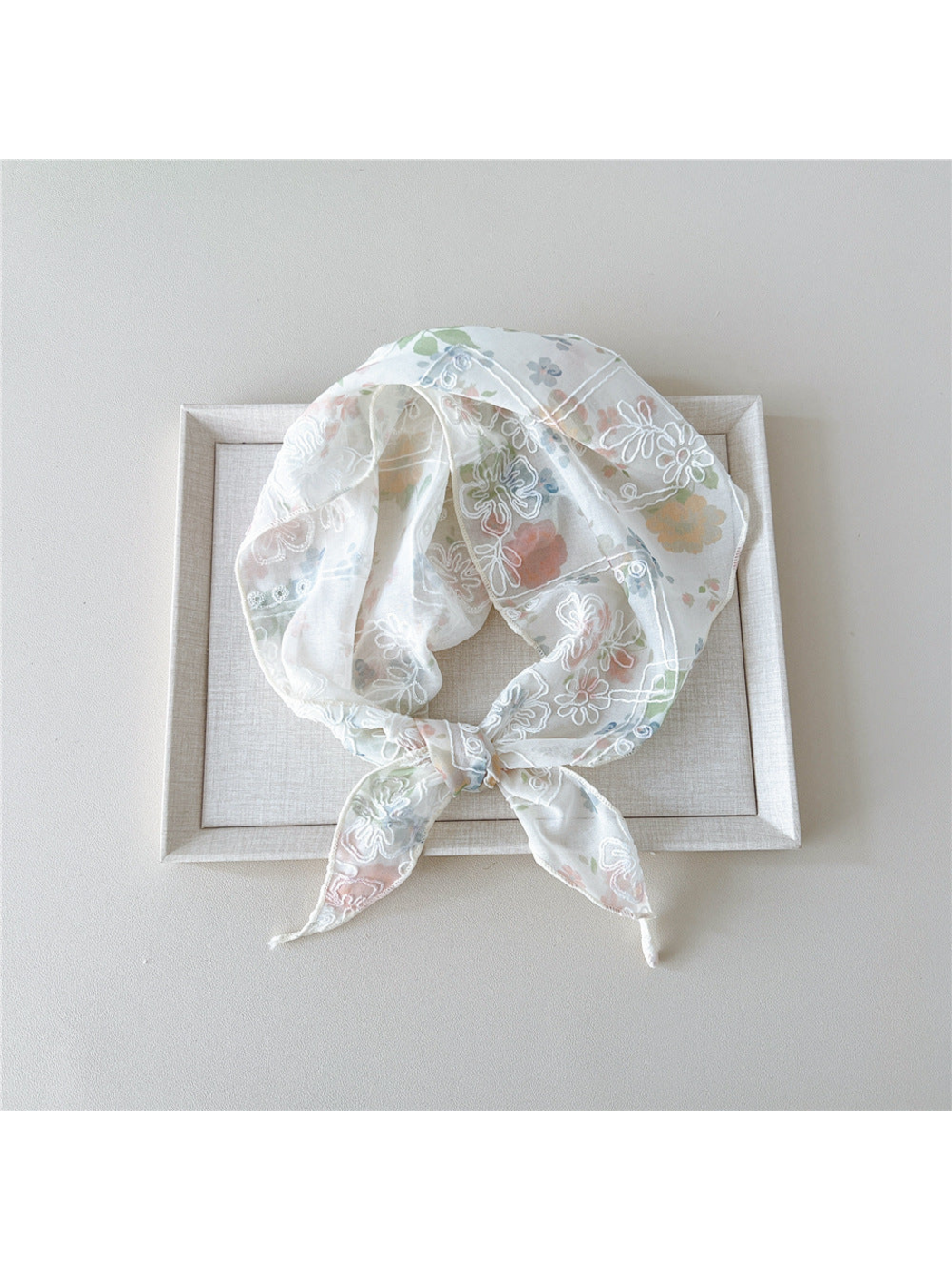 Pink floral scarf with white embroidery tied in a loop on a tray