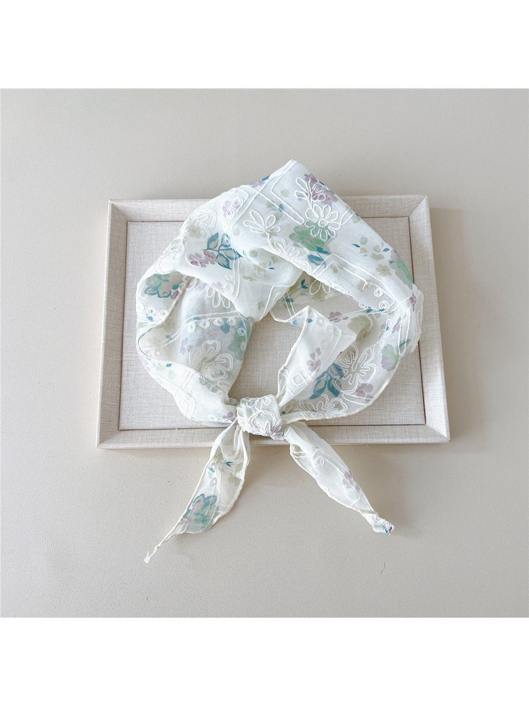 Green floral scarf with white embroidery tied in a loop on a tray