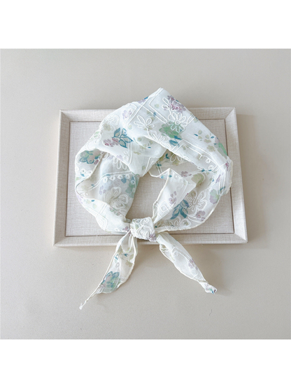 Green floral scarf with white embroidery tied in a loop on a tray
