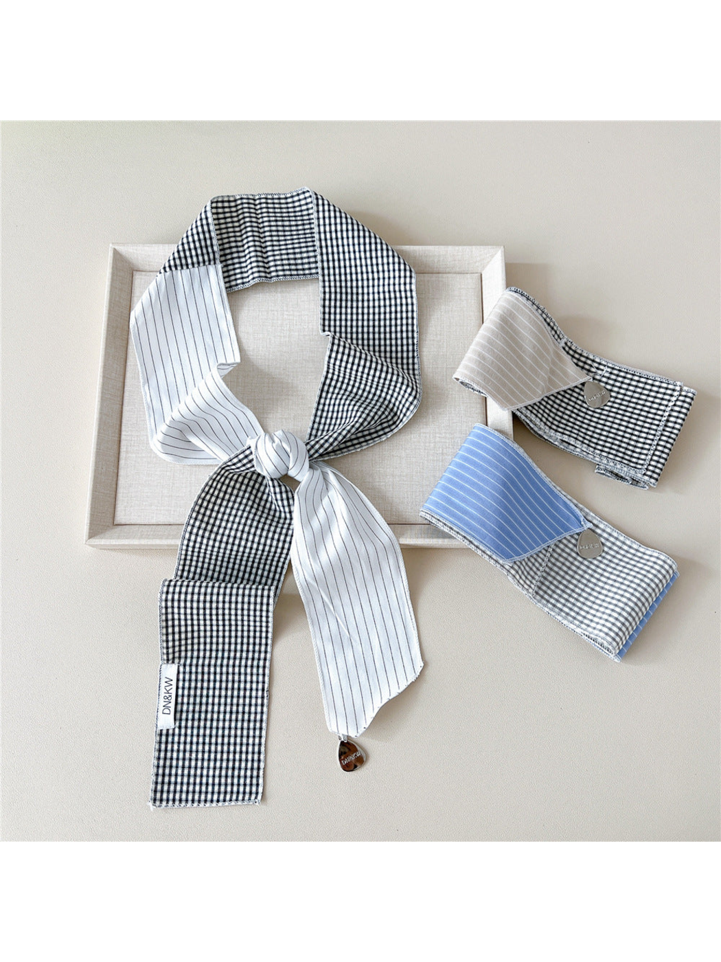 White scarf in a knotted loop beside folded Beige and Blue scarves