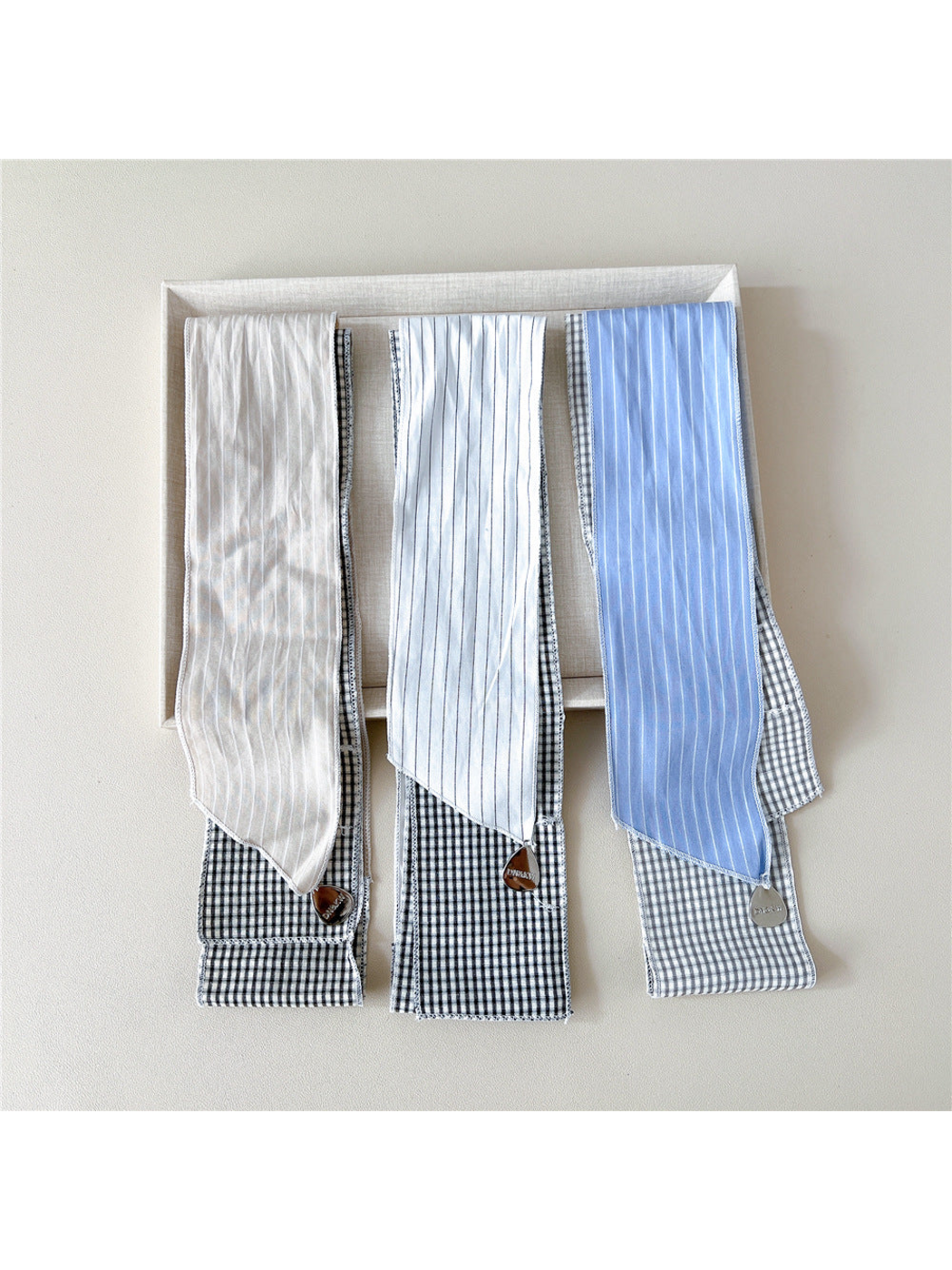 Beige, White and Blue scarves folded side by side with striped ends and teardrop charms