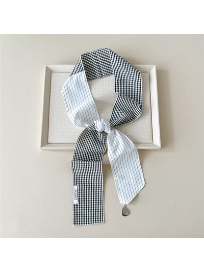 White scarf with gingham checks and narrow stripes tied in a loop with a teardrop charm