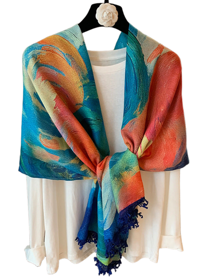 Blue scarf with multicolored painterly swirls and dark blue fringe, knotted over a white top