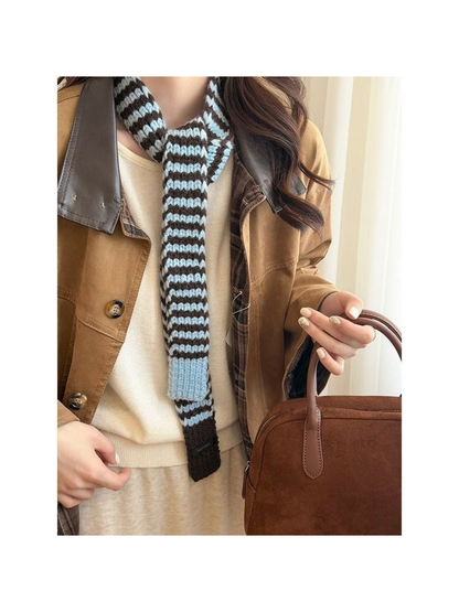 Blue striped knit scarf with light blue and dark brown end panels, worn with a brown jacket