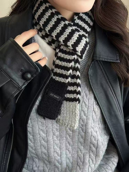Gray striped knit scarf with contrasting end panels, knotted above a cable-knit sweater