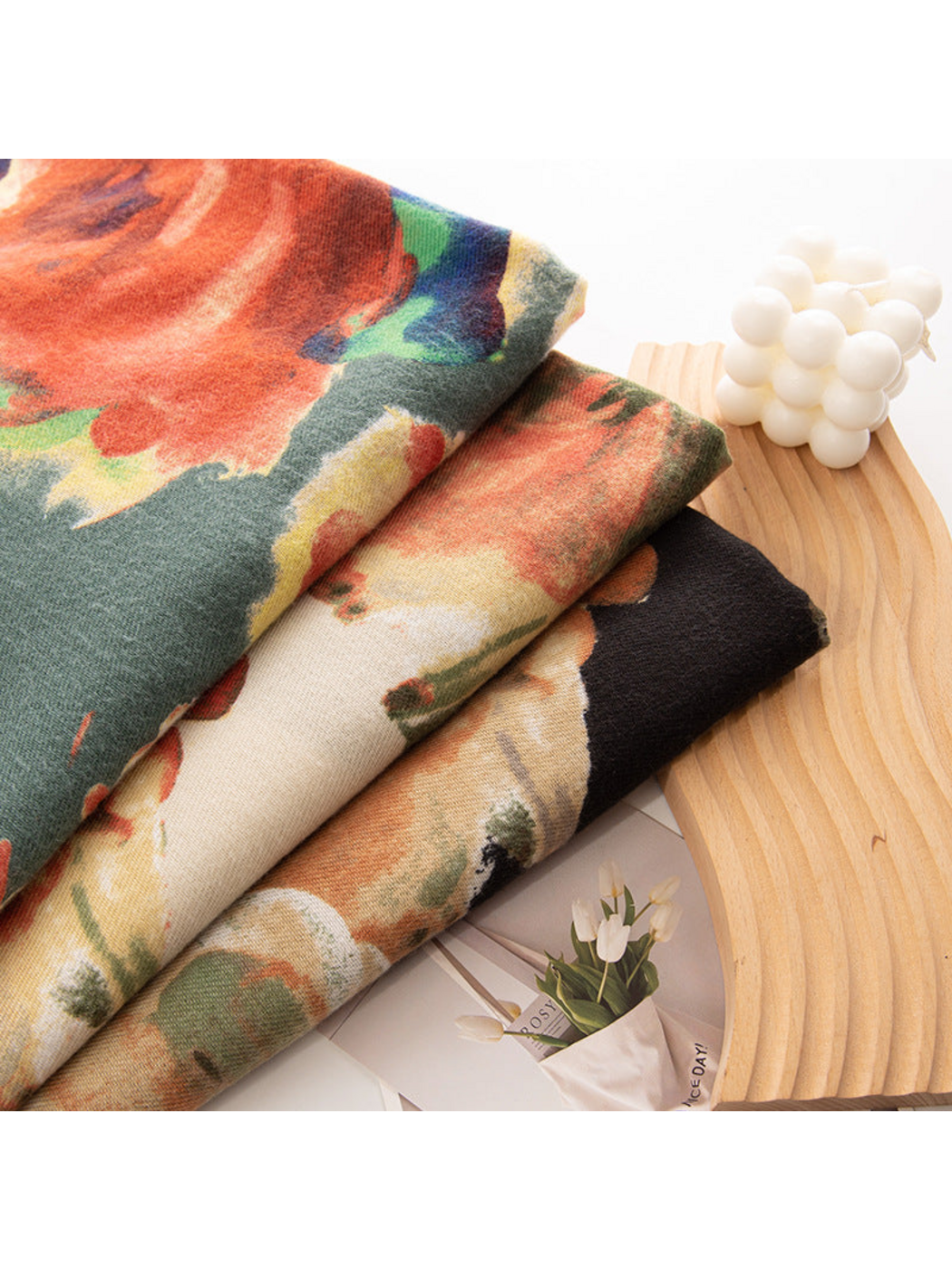 Close-up of three overlapping floral scarves beside a wooden tray