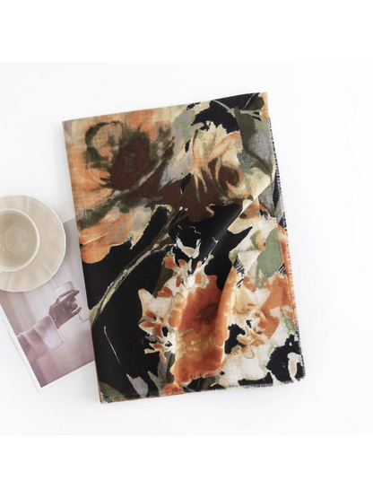 Black floral scarf folded on a white surface beside a cup and magazine