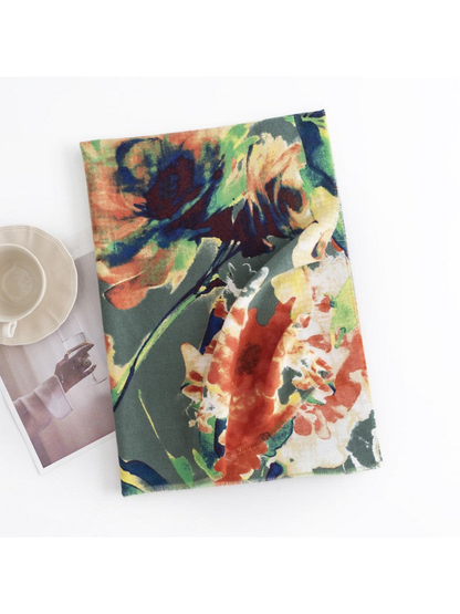 Green floral scarf folded on a white surface beside a cup and magazine