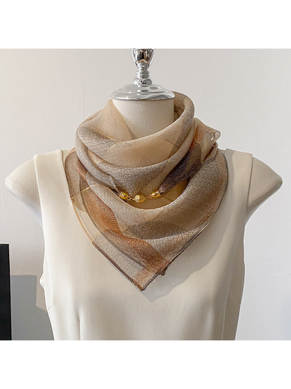 Scarf wrapped around a mannequin neck with a triangular front and gold-tone ornaments